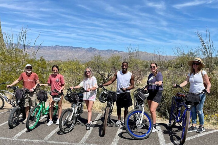 A group of people with bicycles in a parking lot with a desert landscape in the background. 2