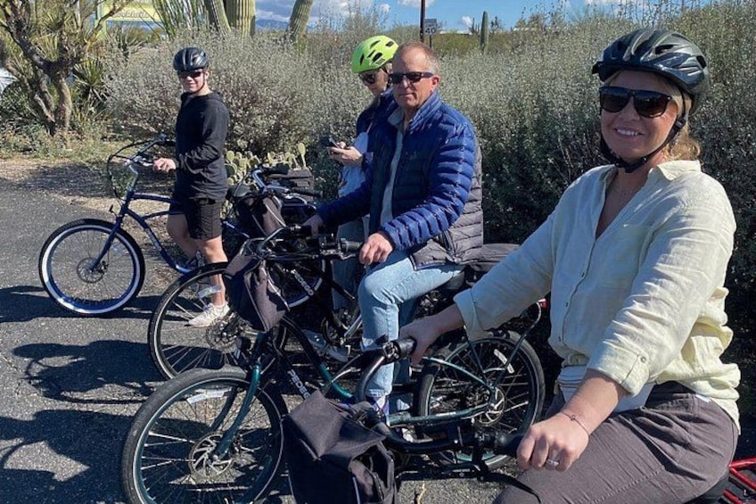 Three people on bicycles, one in a wheelchair, in a desert-like environment with sparse vegetation. 5