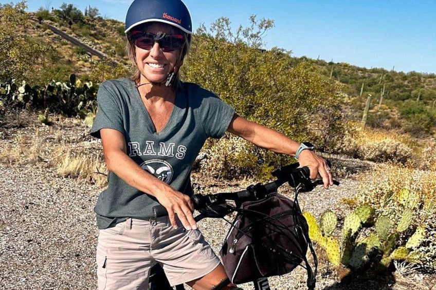A person on a bicycle with a backpack, wearing a helmet, in a desert-like environment with sparse vegetation and a clear sky. 4