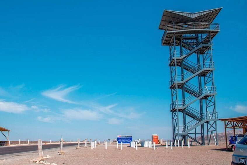 A tall metal tower with a staircase, a clear blue sky, and a road with white posts. 1