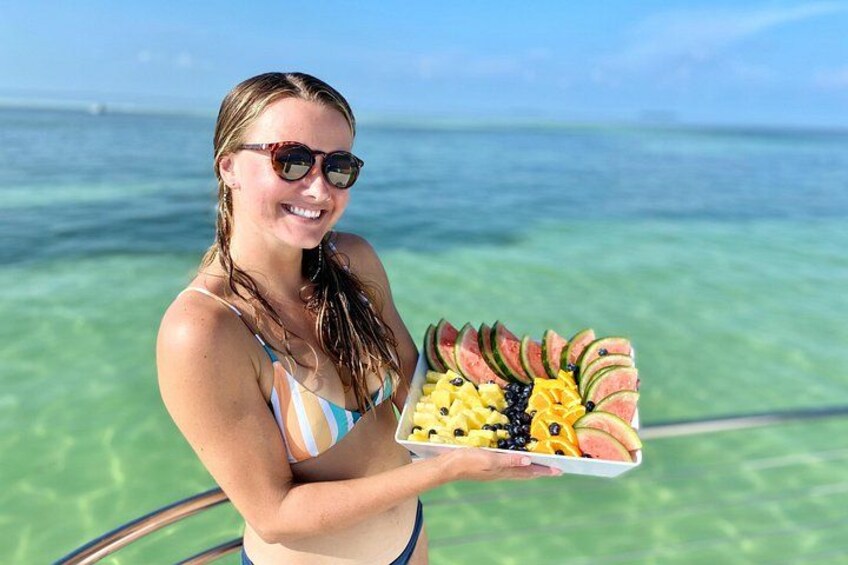 A person holding a tray of fruit by a body of water. 5