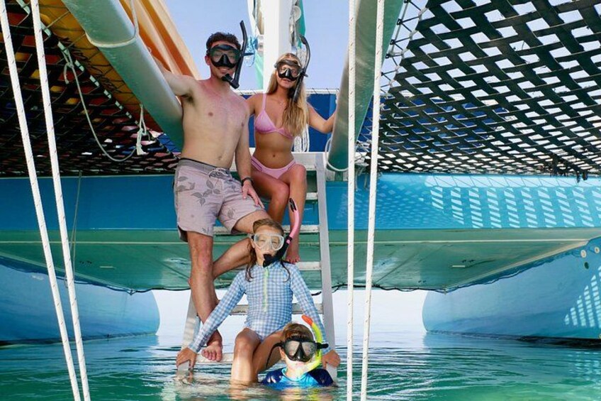 A boat with people wearing snorkeling gear, a ladder, and a shaded area. 4