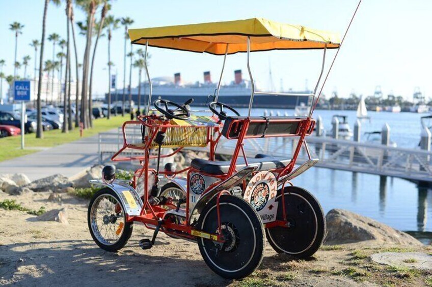 A red and yellow beach cart parked on a sandy area near a marina with boats and a city skyline in the background. 1