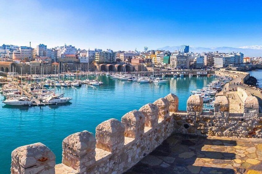 A coastal cityscape with a harbor filled with boats, a stone wall, and a clear blue sky. 2