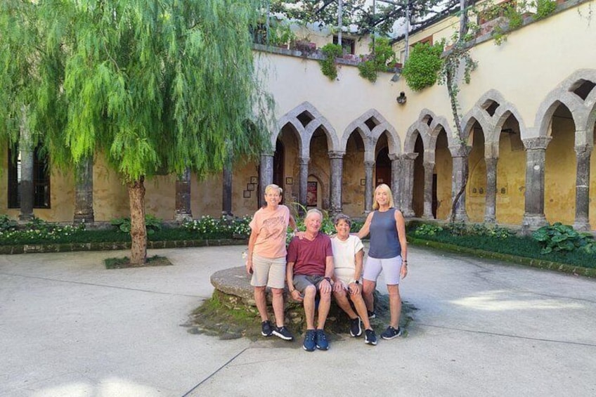 A courtyard with a tree, a stone bench, and a building with arched windows. 5