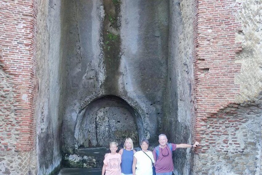 A group of people standing in front of a large stone archway with a brick wall on either side. 4
