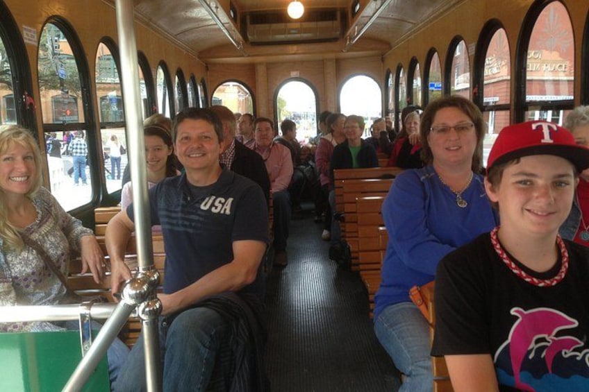 A bus interior with passengers seated, windows, and a metal pole. 2