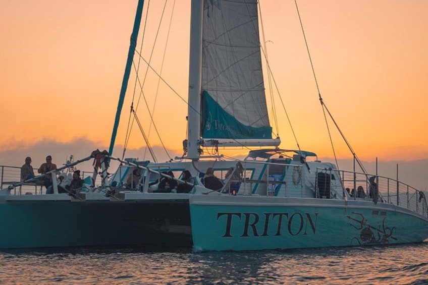 A sailboat named TRITON with people on deck during sunset. 3