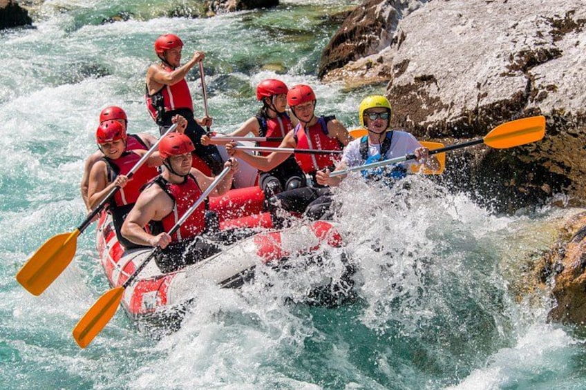 A group of people in a red and white raft navigating through a river with rapids. 3