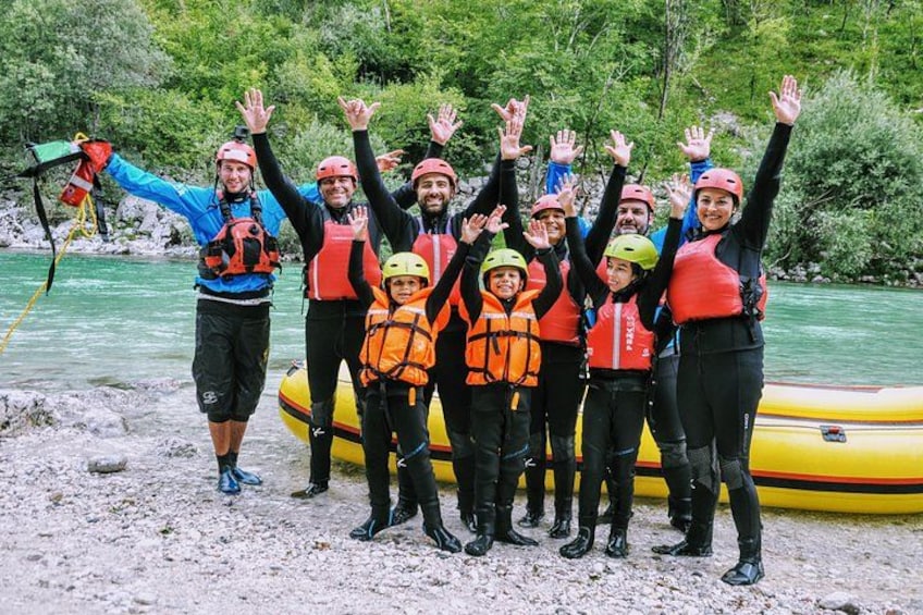 A group of people wearing life jackets and helmets, standing by a yellow raft on a riverbank. 2