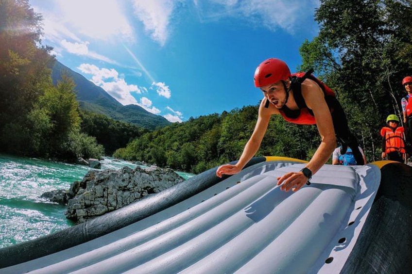 A person in a red helmet and life jacket on a raft, with a river and mountains in the background. 5