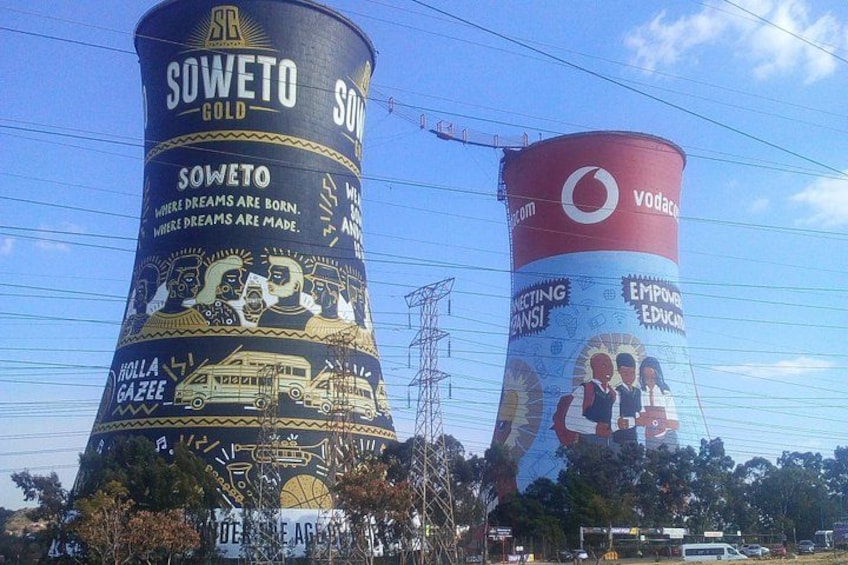 Deux grandes tours d’eau ornées de publicités, l’une pour la marque Soweto Gold et l’autre pour Vodacom, avec un ciel dégagé en arrière-plan. 1
