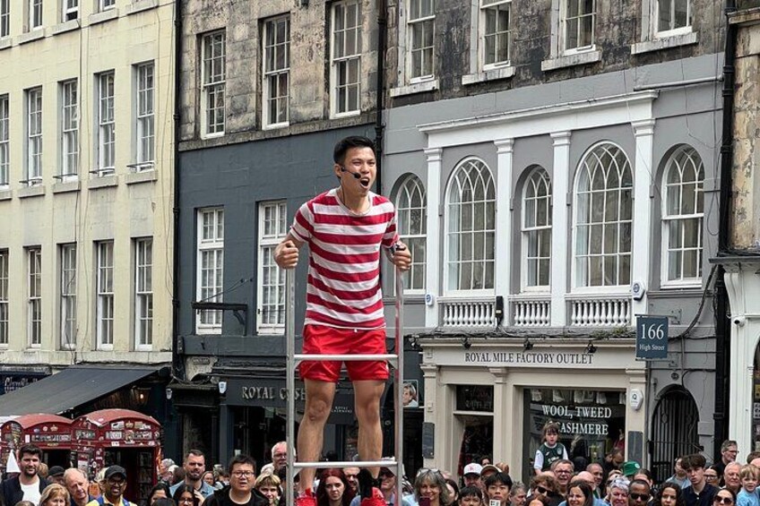 Una persona equilibrista camina sobre una cuerda floja en una calle concurrida, con edificios históricos al fondo. 3