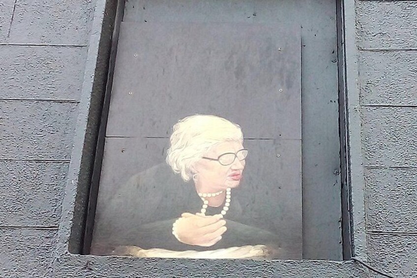 A mural of a person with white hair, wearing a pearl necklace, on a gray wall. 2