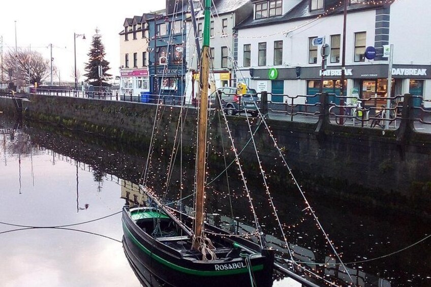 A green boat docked at a pier with buildings and a bridge in the background. 5