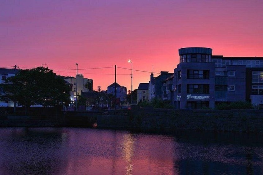 A sunset over a cityscape with buildings reflecting on water. 4