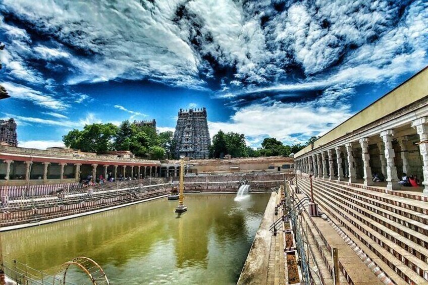 A temple complex with a large water body, a tower, and a covered walkway. 3