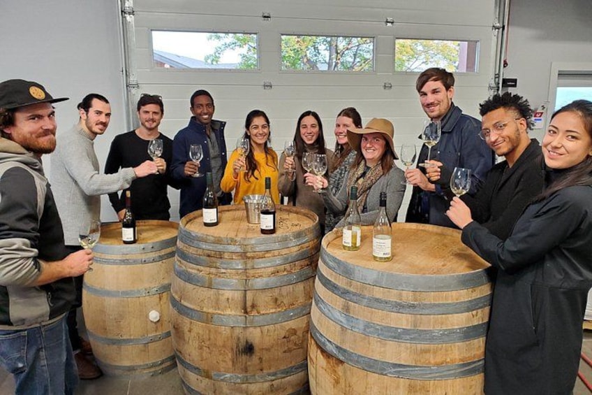 A group of people standing around large wooden barrels, holding wine glasses. 2