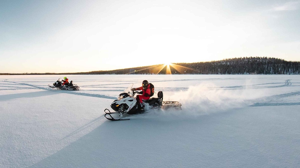 Dos motos de nieve sobre un lago congelado, con el sol poniéndose al fondo. 1