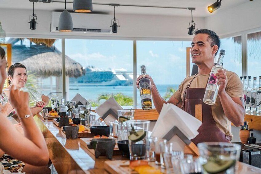 A bar with a view of the ocean, a bartender holding a bottle, and a customer seated at the bar. 5