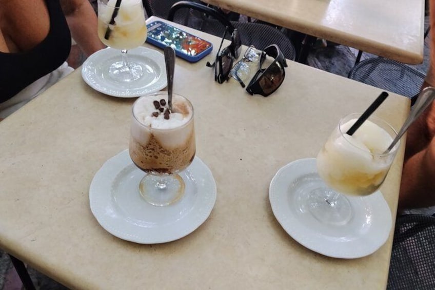 A table with two drinks on white plates, one with coffee and the other with a lighter-colored beverage, both with straws. 3