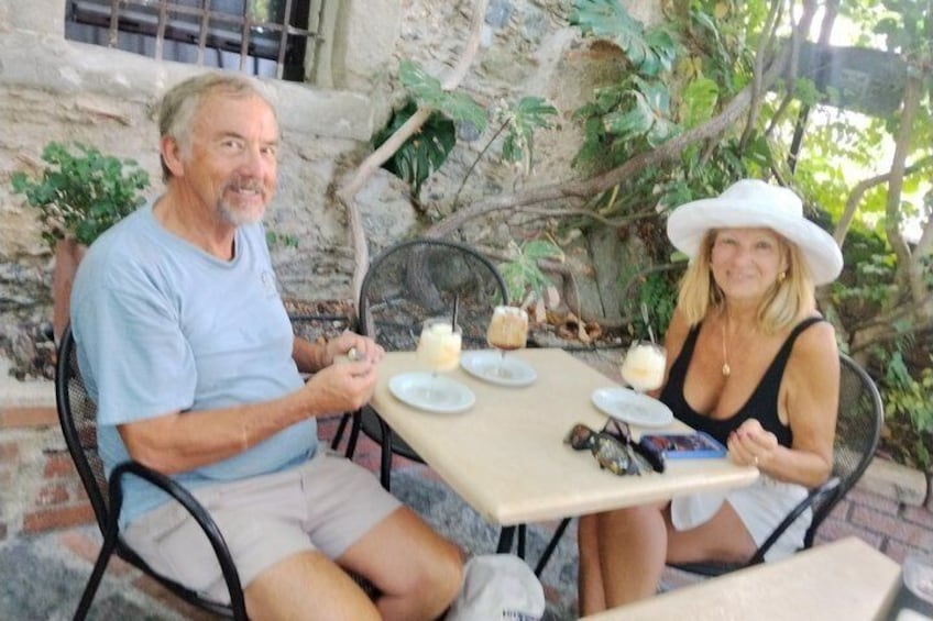 Two people seated at an outdoor table with plates, cups, and a book. 2