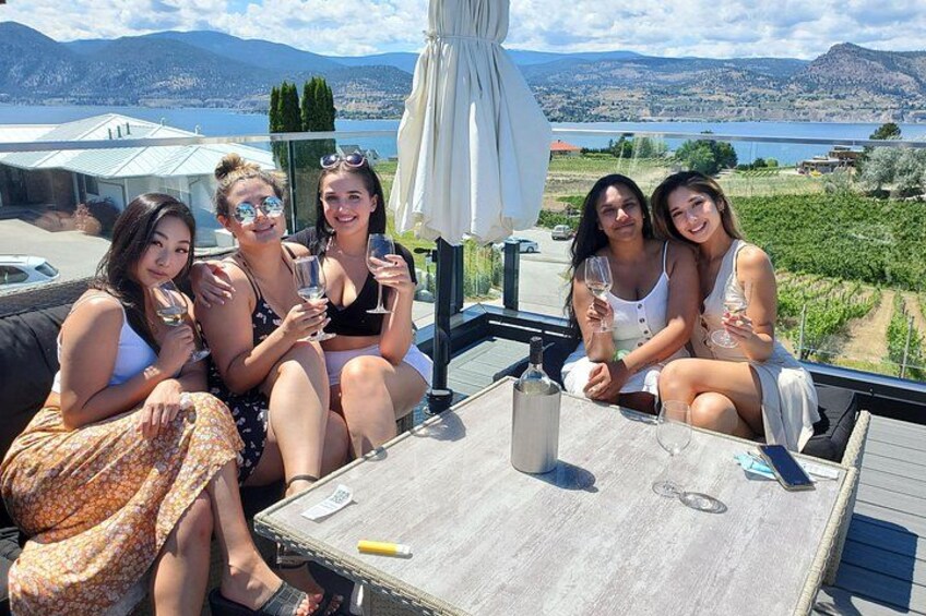 Un groupe de personnes est assis sur une terrasse, autour d’une table, et profite d’une vue panoramique sur un paysage magnifique, avec des montagnes et une étendue d’eau. 3