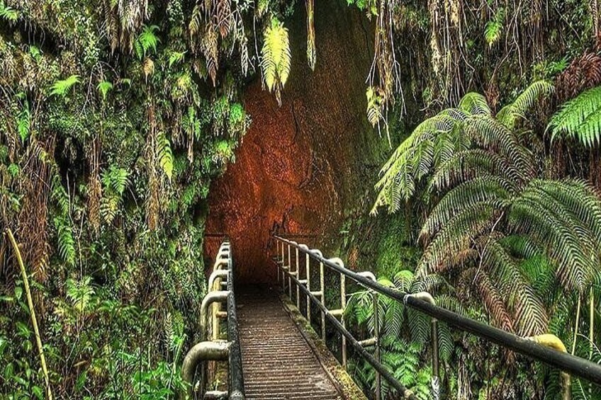 A wooden bridge with metal railings leading into a cave with a red rock face. 1