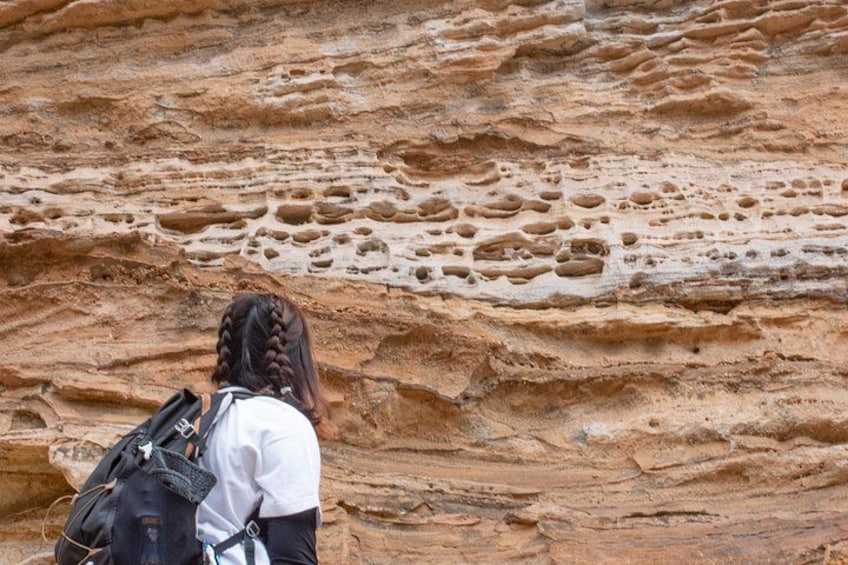 Eine Person mit Zöpfen und einem Rucksack steht vor einer Felsformation mit deutlichen Erosionsspuren. 4