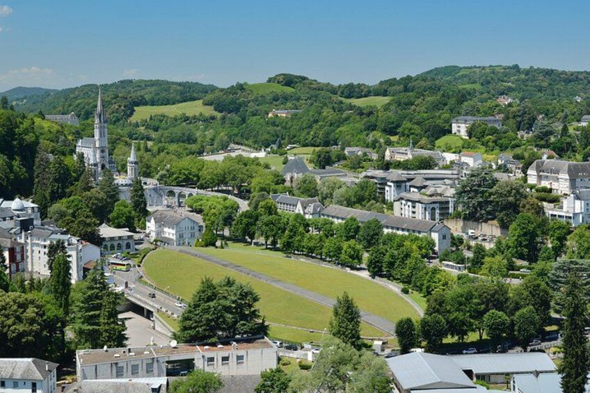 A town with a large green field, a church with a tall steeple, and residential buildings. 1