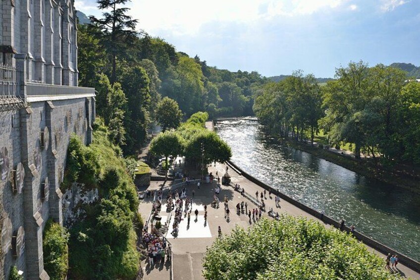 A riverside walkway with people walking, a historic building, and lush greenery. 5