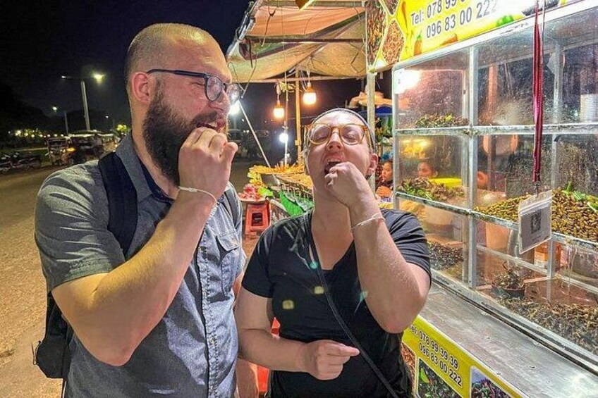 Two people tasting food at a street food stall. 1