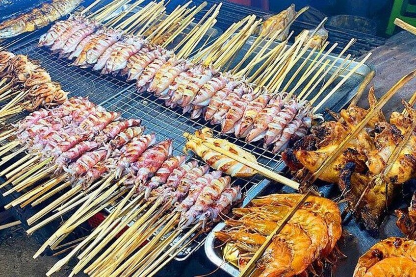 A variety of skewered seafood and meats grilling on a metal rack. 5