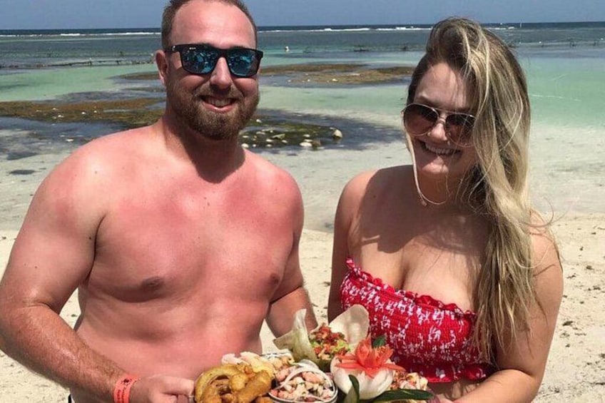 Une scène de plage avec une eau turquoise et limpide, un rivage sablonneux et une personne tenant une assiette de nourriture. 2