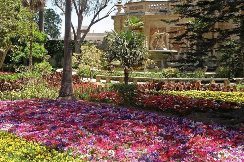 Un jardín con flores coloridas, una fuente y una estatua al fondo. 2