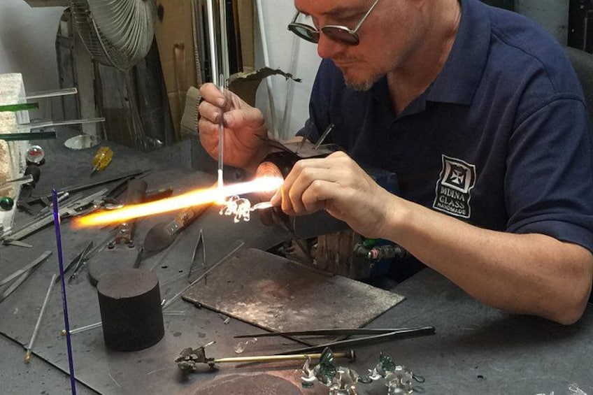 A person working with a torch and metal pieces, possibly a blacksmith or metalworker, in a workshop with tools and equipment. 4