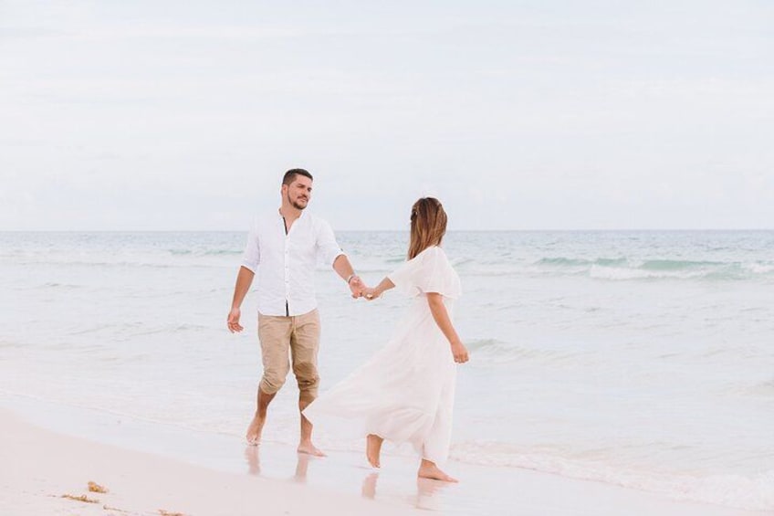A couple walking hand in hand on a beach with the ocean in the background. 1