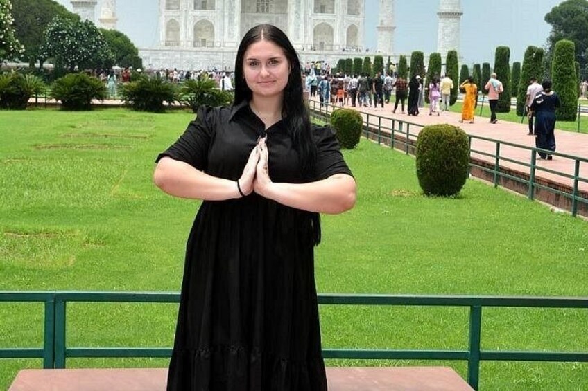 A person in a black dress standing with hands together in front of the Taj Mahal. 5