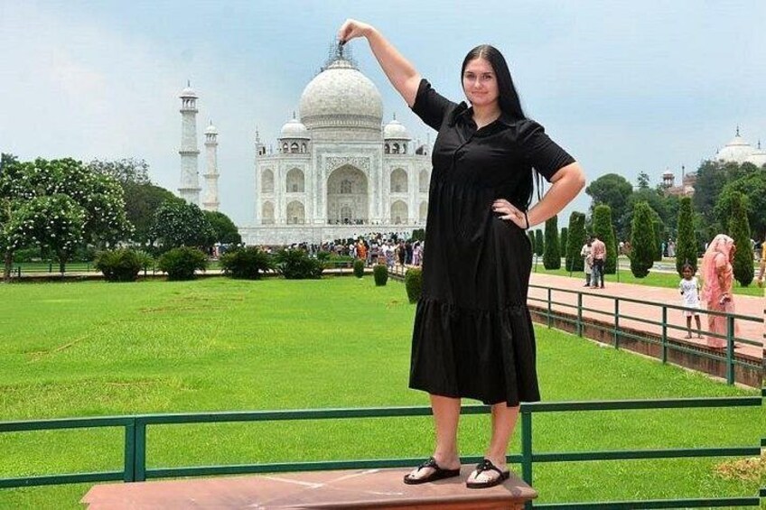 A person standing in front of the Taj Mahal with a green lawn and white marble structure in the background. 3