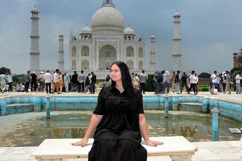 A person in black attire seated on a platform with the Taj Mahal in the background. 2
