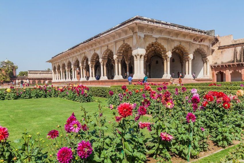 A historic building with arches and a garden with pink flowers. 2