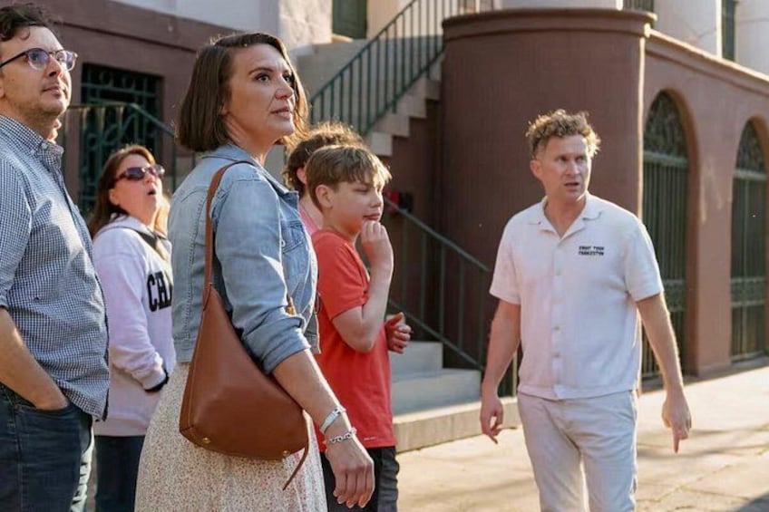 A group of people standing on a sidewalk, a building with arched windows, and a staircase. 4