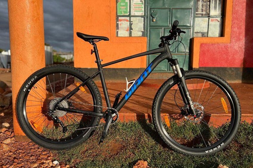 A mountain bike parked next to a pillar with a building in the background. 2