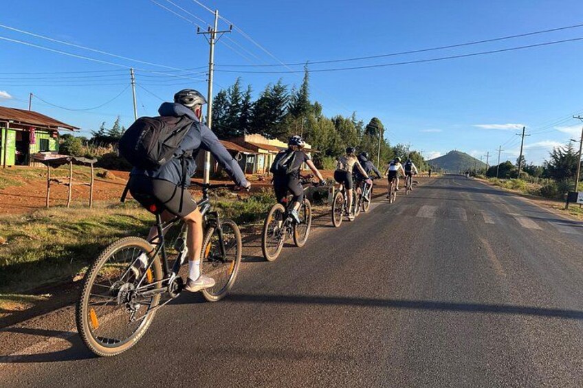 A group of cyclists on a paved road with houses and trees in the background. 5