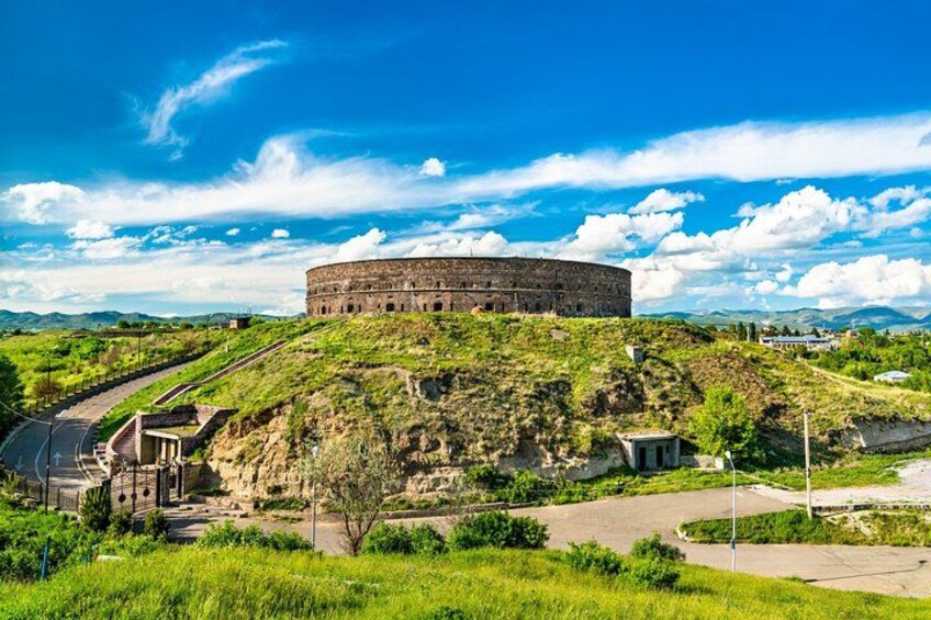A large circular building on a hill with a clear sky. 2