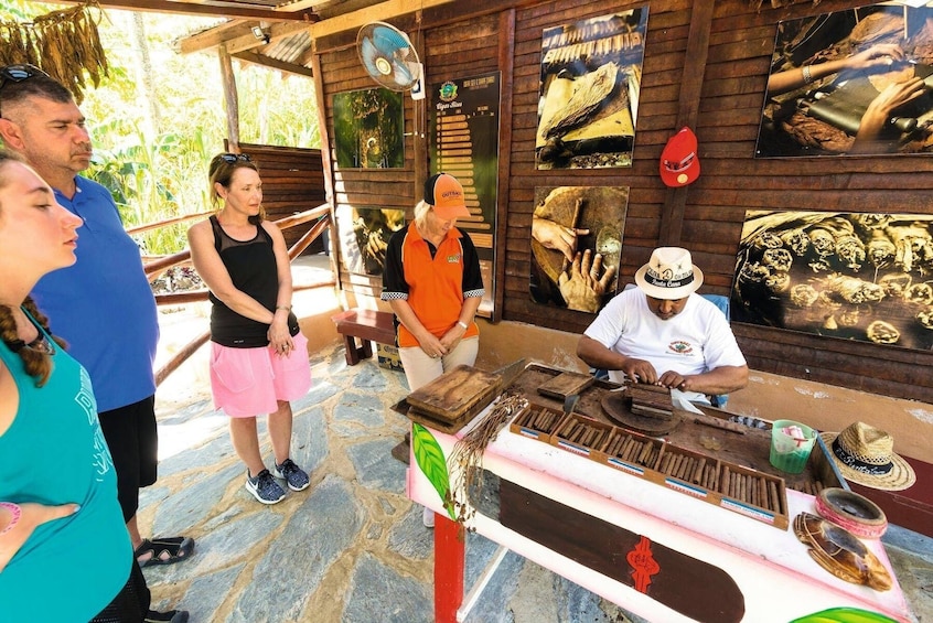 A group of people observing a cigar-making process at a wooden workshop. 1