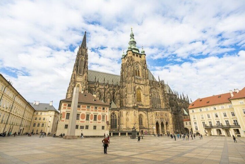 En stor katedral med et højt spids og et tårn med et ur i midten af et torv omgivet af historiske bygninger. 1