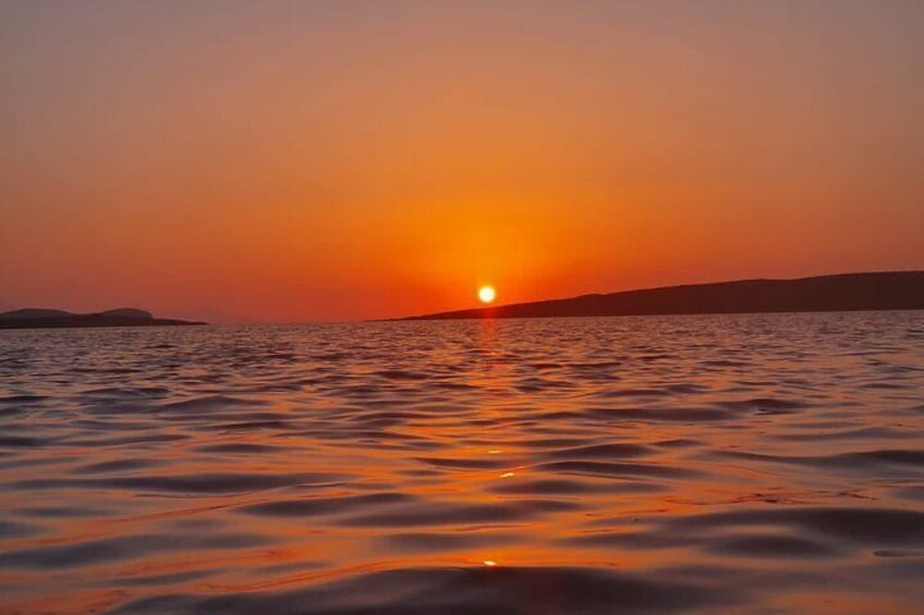 Un coucher de soleil sur une étendue d’eau calme, avec la silhouette d’une terre lointaine à l’horizon. 1