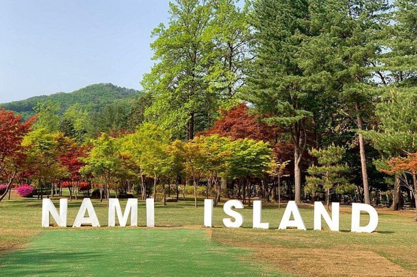 A sign with 'NAMI ISLAND' in large letters, surrounded by trees and a grassy area. 2