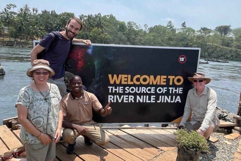 A group of people posing in front of a sign that reads 'WELCOME TO THE SOURCE OF THE RIVER NILE JINJA.' 1